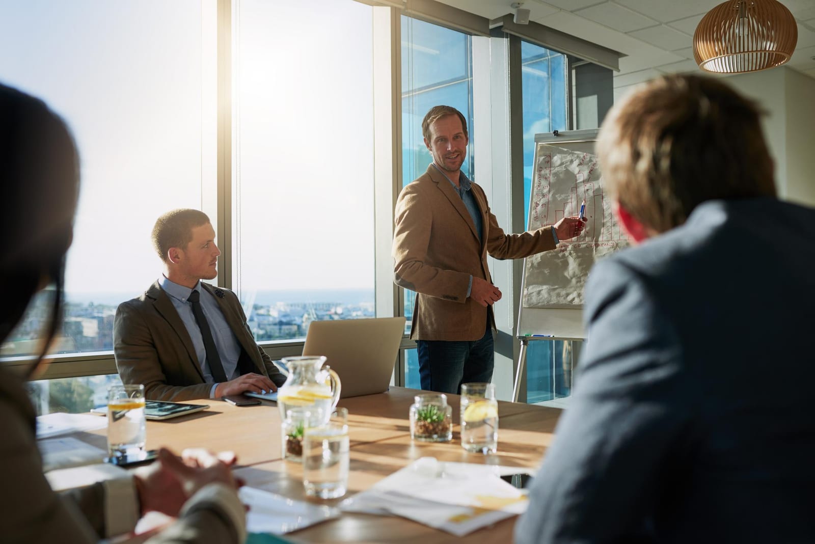 Ein Mann im Jackett präsentiert drei sitzenden Kolleginnen und Kollegen ein Flipchart in einem hellen Besprechungsraum.